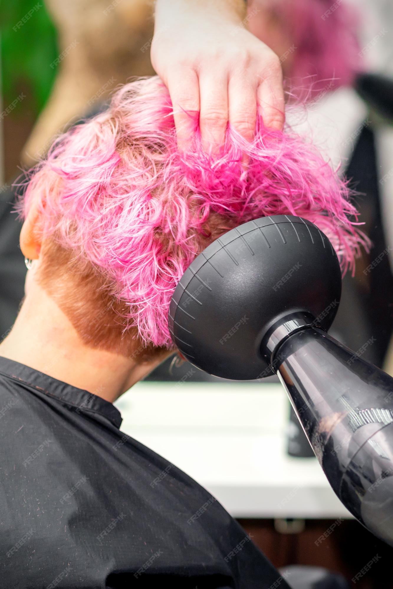 Secador de cabelo preto na mão de uma mulher em um fundo rosa