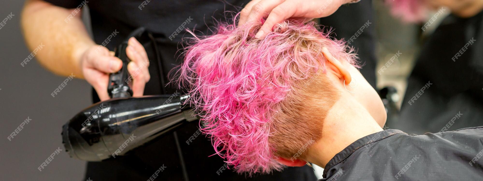 Secador de cabelo preto na mão de uma mulher em um fundo rosa