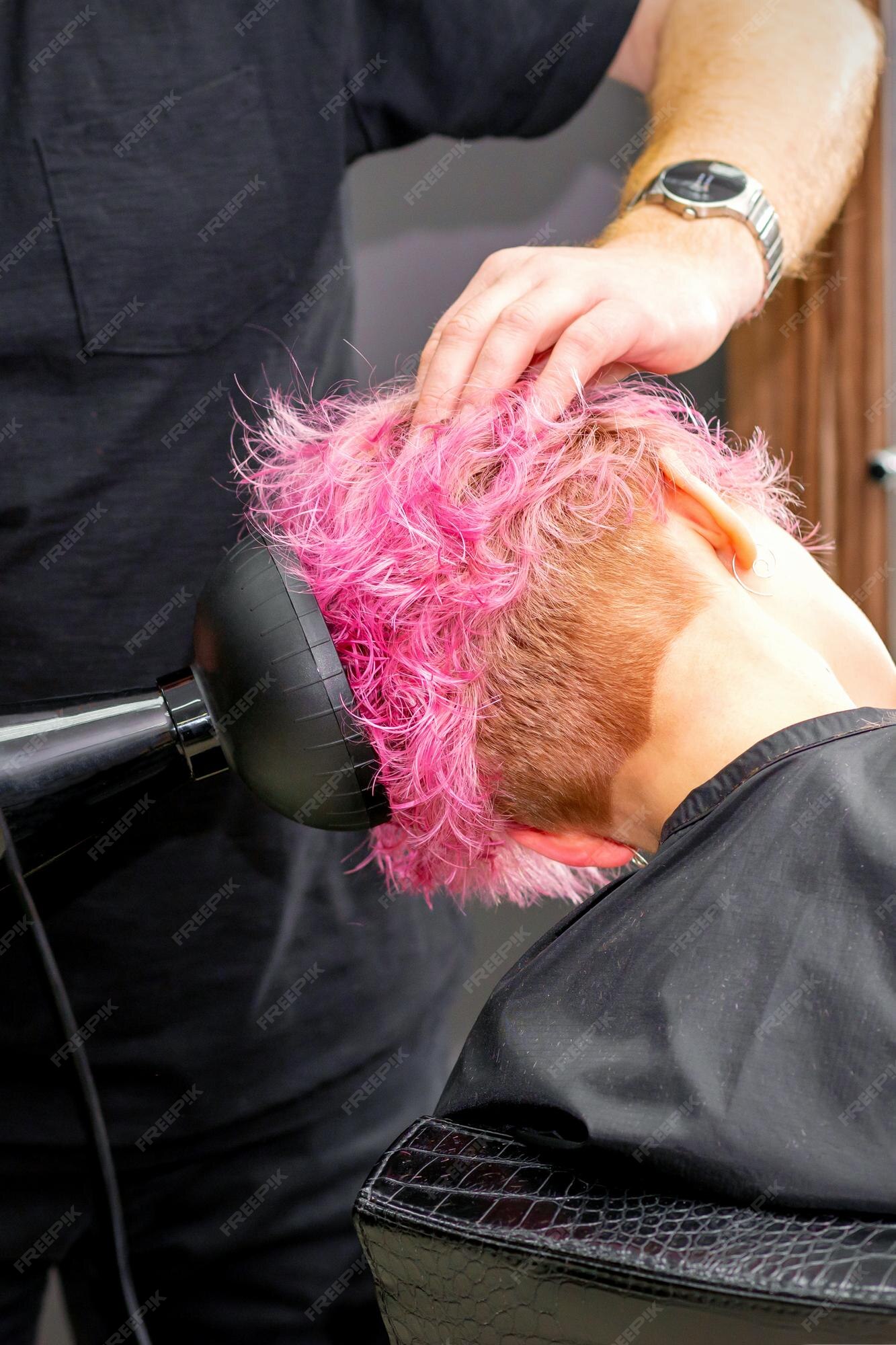 Secador de cabelo preto na mão de uma mulher em um fundo rosa