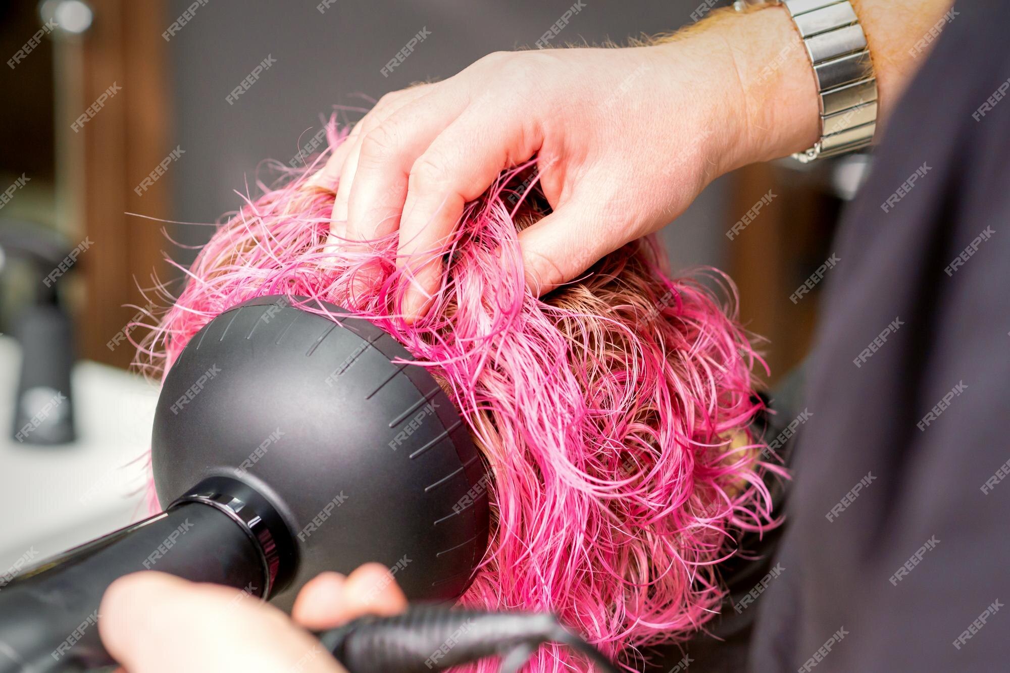 Secador de cabelo preto na mão de uma mulher em um fundo rosa