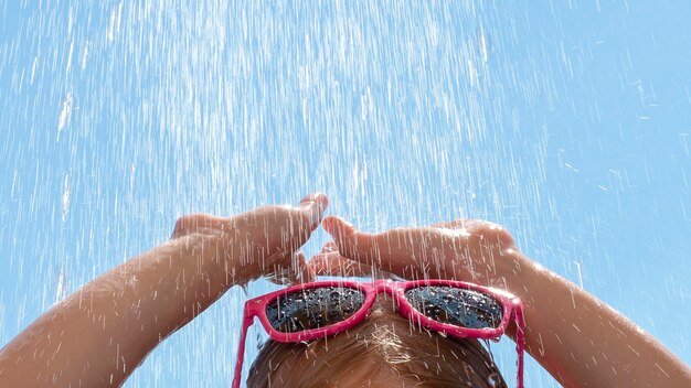 Foto seção alta de menina com óculos de sol sob o chuveiro