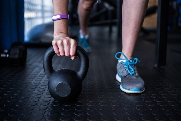 Seção baixa de atleta feminina segurando kettlebell no ginásio