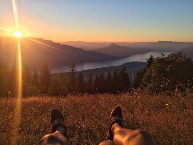 Foto seção baixa de homem na montanha contra o céu durante o pôr-do-sol