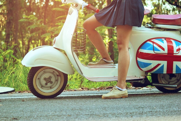 Seção baixa de mulher de pé junto a uma scooter na estrada