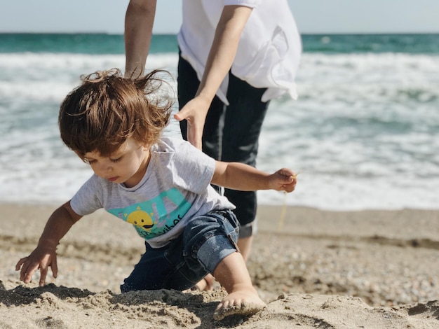 Seção baixa de mulher segurando menino brincando na areia na praia