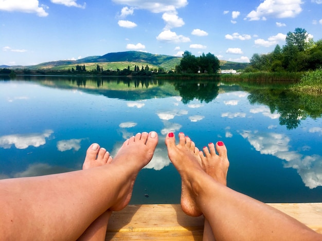 Foto seção baixa de mulheres relaxando na beira do lago contra o céu