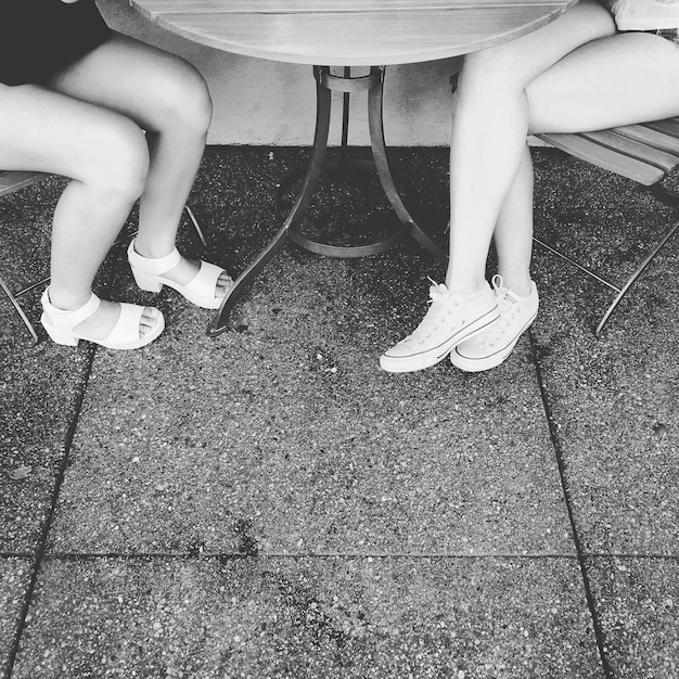 Foto seção baixa de mulheres sentadas em cadeiras à mesa em um café na calçada
