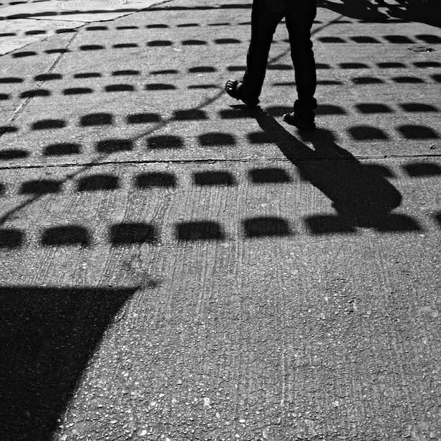 Foto seção baixa de pessoa andando na rua com sombras de bandeira