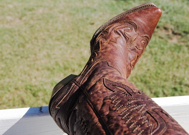 Foto seção baixa de pessoa vestindo botas de cowboy castanhas em cerca de madeira