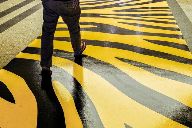 Foto seção baixa de um homem caminhando em uma passagem de zebra com padrões