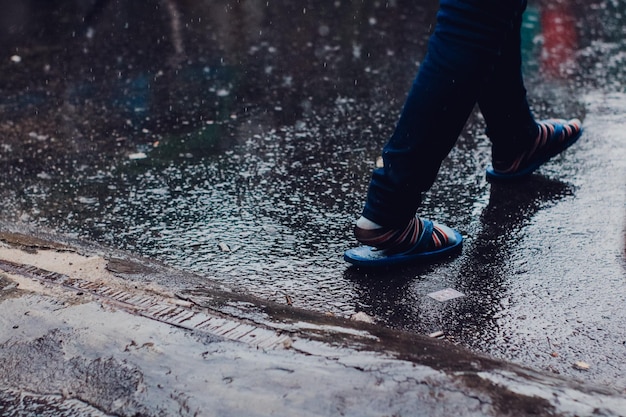 Seção baixa de um homem caminhando na estrada durante a chuva
