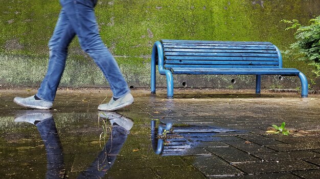 Foto seção baixa de um homem caminhando por um banco azul refletindo em uma poça