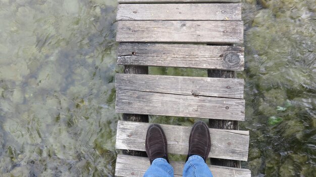 Seção baixa de um homem de pé em uma ponte de madeira sobre o rio