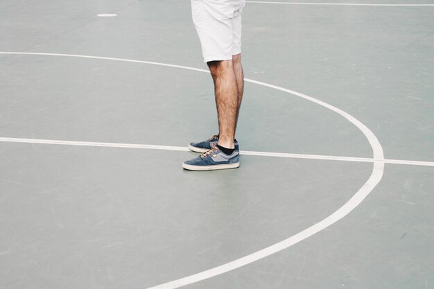 Seção baixa de um homem de pé em uma quadra de basquete