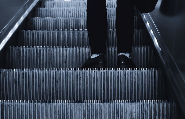 Seção baixa de um homem de pé na escada rolante