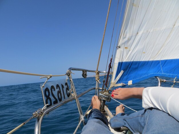 Seção baixa de um homem em um veleiro navegando no mar contra um céu azul claro