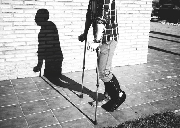 Foto seção baixa de um homem ferido caminhando com a ajuda de muletas na calçada