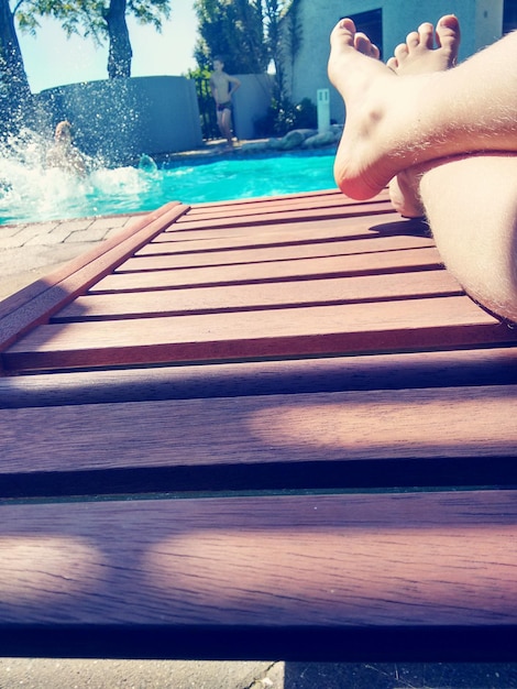 Foto seção baixa de um homem relaxando em uma cadeira de terraço à beira da piscina