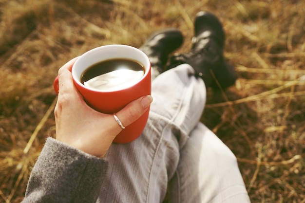 Seção baixa de um homem segurando uma xícara de café enquanto está sentado em um campo gramado