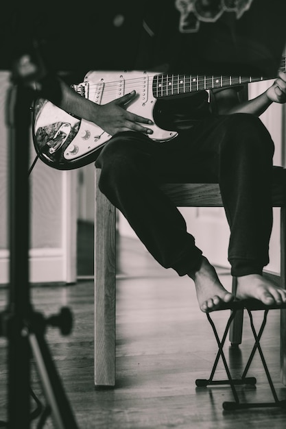 Foto seção baixa de um homem tocando guitarra enquanto está sentado em uma cadeira em casa