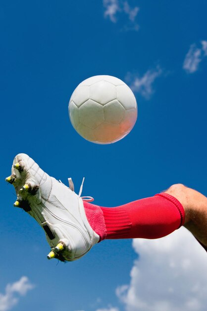 Foto seção baixa de um jogador de futebol chutando a bola contra o céu azul