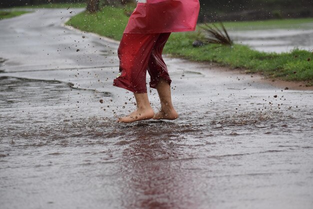 Foto seção baixa de um menino de pé na estrada molhada durante a estação chuvosa