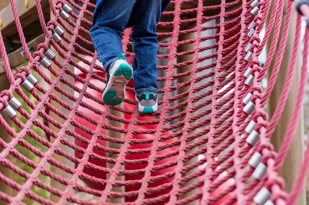 Seção baixa de um menino escalando uma corda vermelha no playground