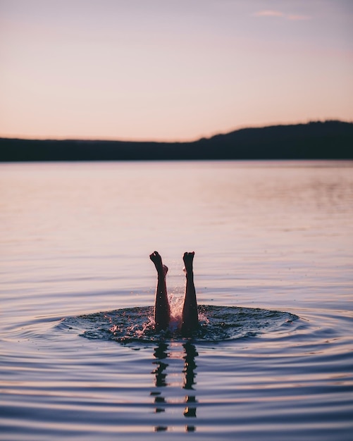 Seção baixa de uma jovem nadando no lago contra o céu ao pôr do sol