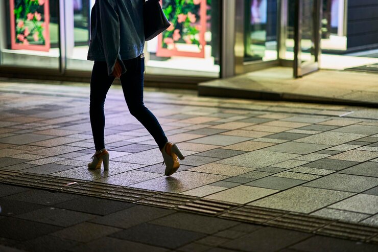 Foto seção baixa de uma mulher caminhando por uma calçada à noite
