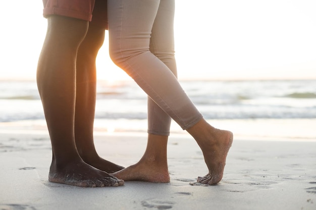 Seção baixa do casal afro-americano abraçando na praia ao pôr do sol. verão, união, romance e férias, inalterados.