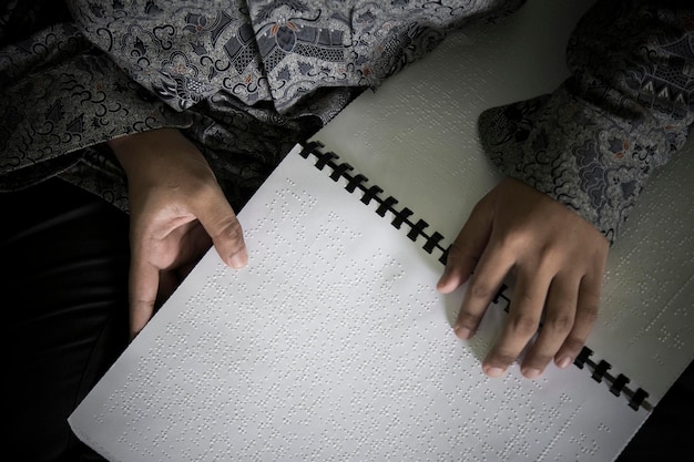 Foto seção central de uma pessoa cega lendo a bíblia em braille