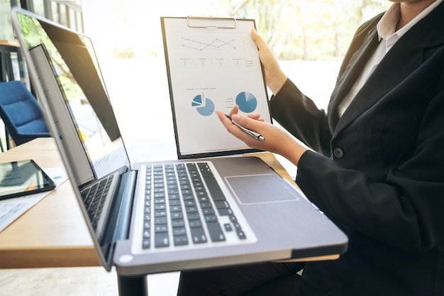 Seção do meio de uma mulher de negócios segurando um clipboard por um laptop na mesa