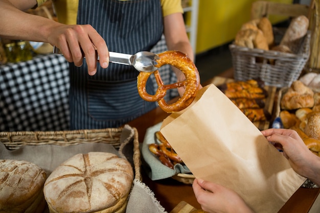 Seção intermediária da equipe embalando pão de pretzel em um saco de papel no balcão