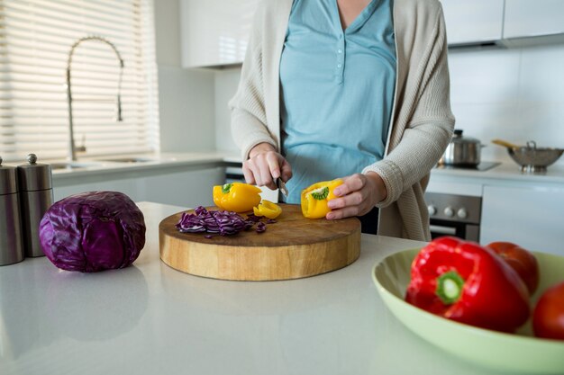 Seção intermediária da mulher cortando pimentão amarelo na cozinha