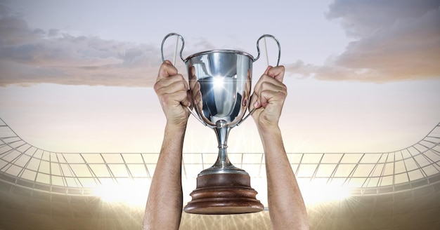 Seção intermediária de um atleta do sexo masculino, caucasiano, levantando um troféu contra holofotes no fundo