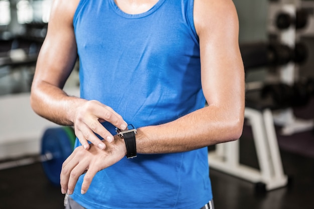 Seção intermediária do homem bonito usando smartwatch no ginásio