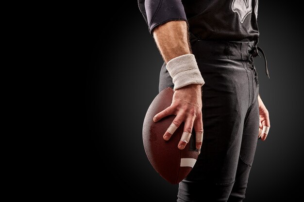 Seção intermediária do jogador de futebol americano com bola contra preto, copie o espaço, vista lateral