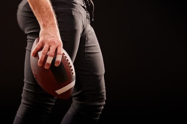 Seção intermediária do jogador de futebol americano com bola contra preto, copie o espaço, vista lateral