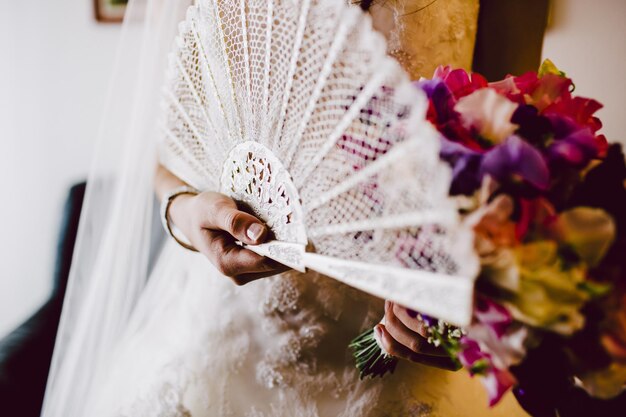 Foto seção média da noiva segurando o ventilador e o buquê de flores