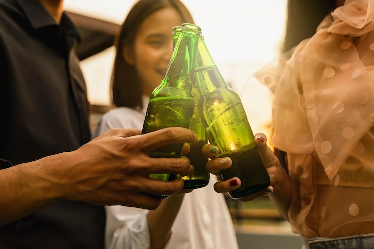 Foto seção média de amigos segurando uma garrafa de cerveja enquanto estão de pé ao ar livre