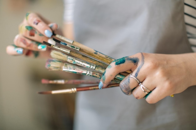 Seção média de artista segurando pincéis de pintura com mãos bagunçadas na oficina