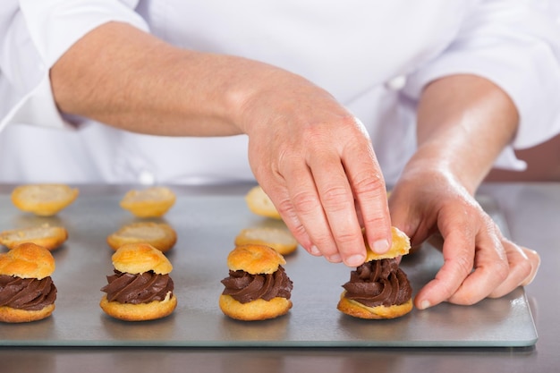 Foto seção média de chef preparando profiteroles em cozinha comercial.