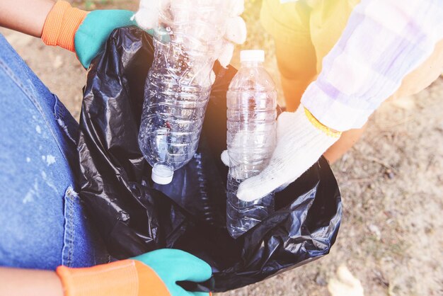 Foto seção média de homem e mulher segurando garrafas em saco de lixo enquanto estão em terra