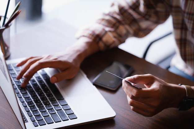 Seção média de homem segurando cartão de crédito e usando laptop na mesa