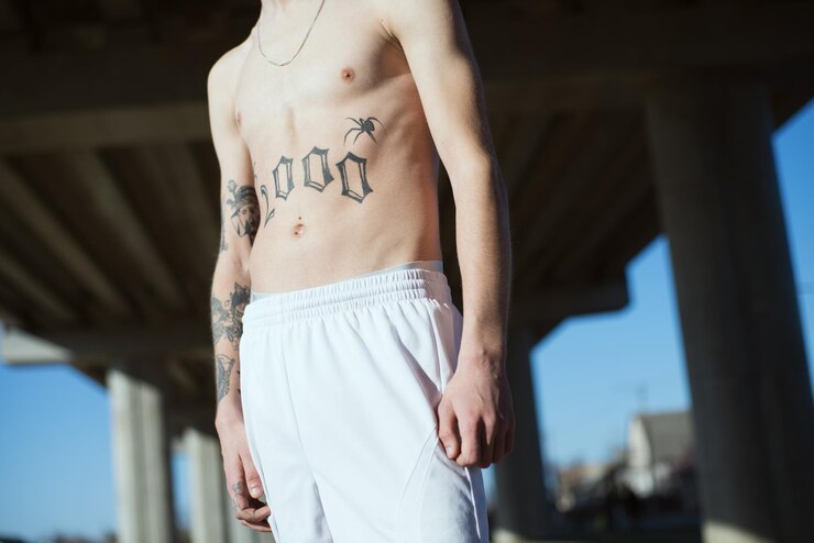 Foto seção média de homem sem camisa com tatuagem de pé ao ar livre
