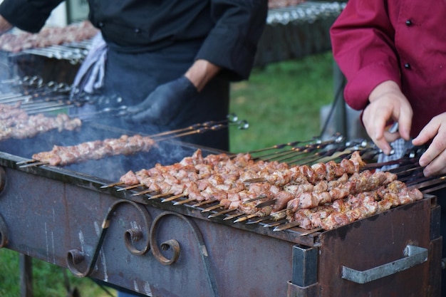 Seção média de homens arranjando espetos de kebab na grelha de churrasco