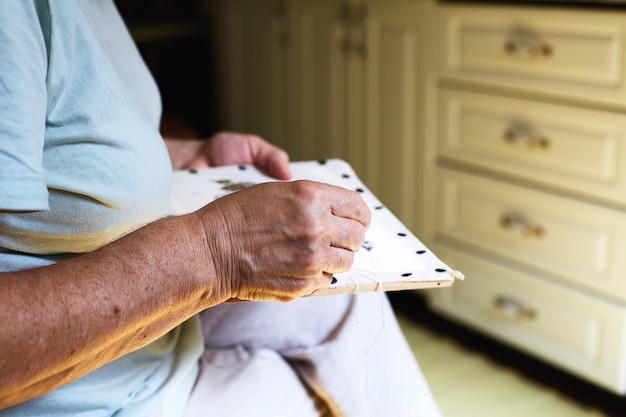 Foto seção média de mãos de mulheres idosas fazendo trabalho de agulha na cozinha de sua casa