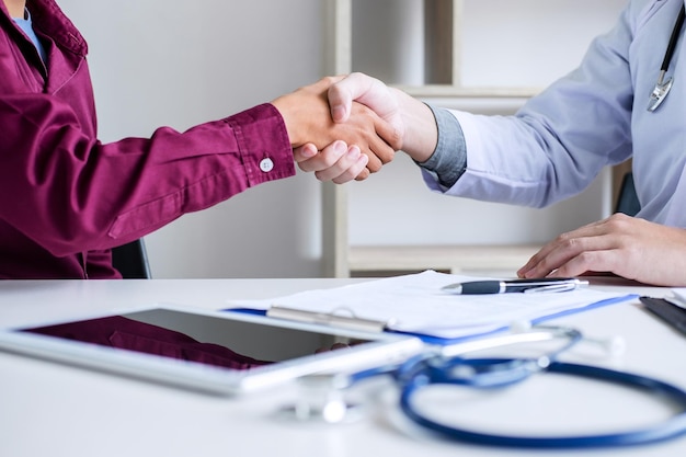 Foto seção média de médico e paciente apertando as mãos sobre a mesa no hospital