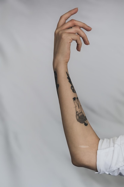 Seção média de mulher com braço tatuado levantado contra fundo branco
