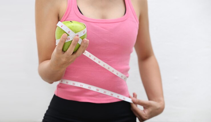 Foto seção média de mulher com maçã e fita métrica de pé contra a parede